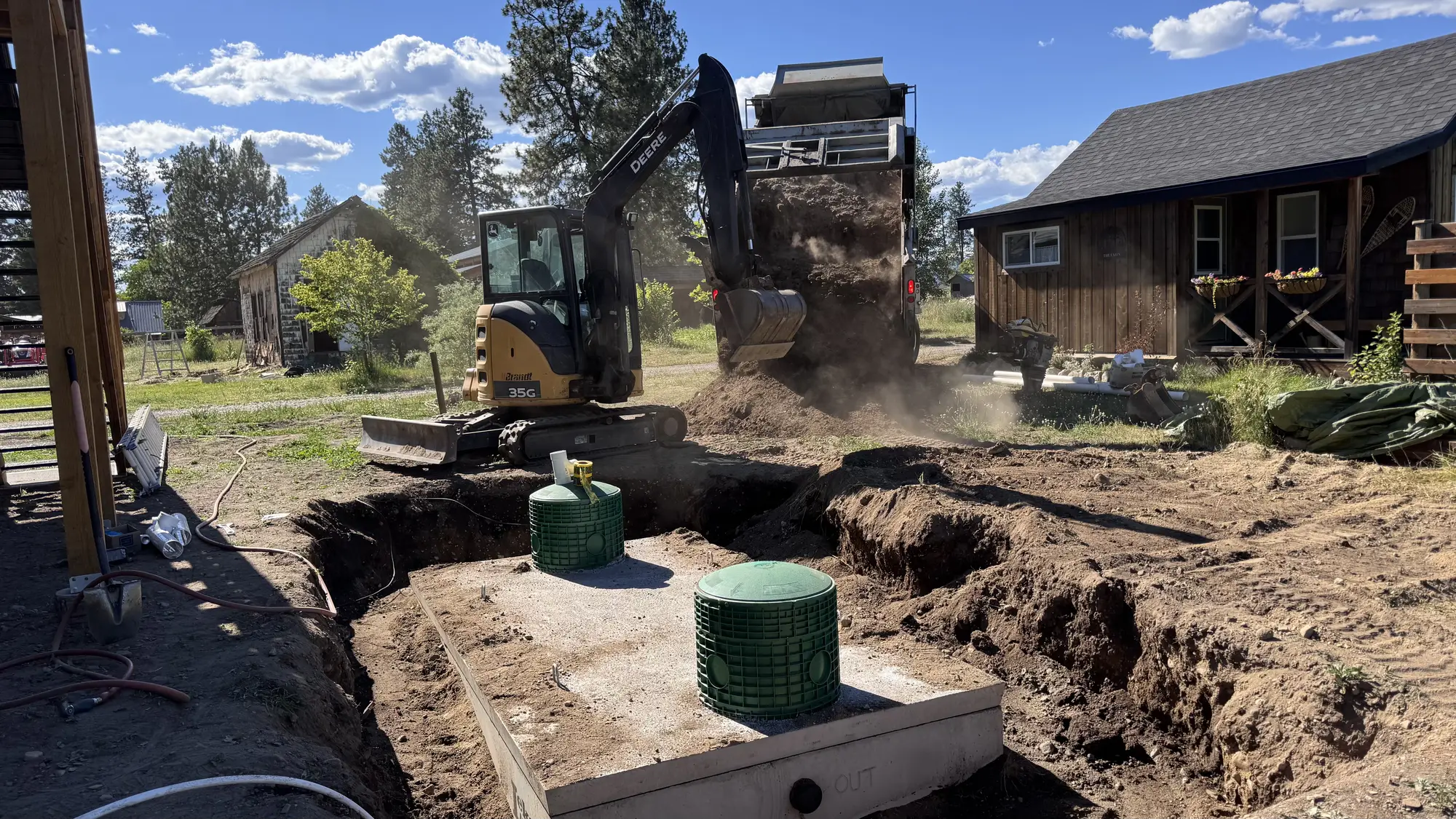 Installed concrete septic tank with green risers and excavation equipment