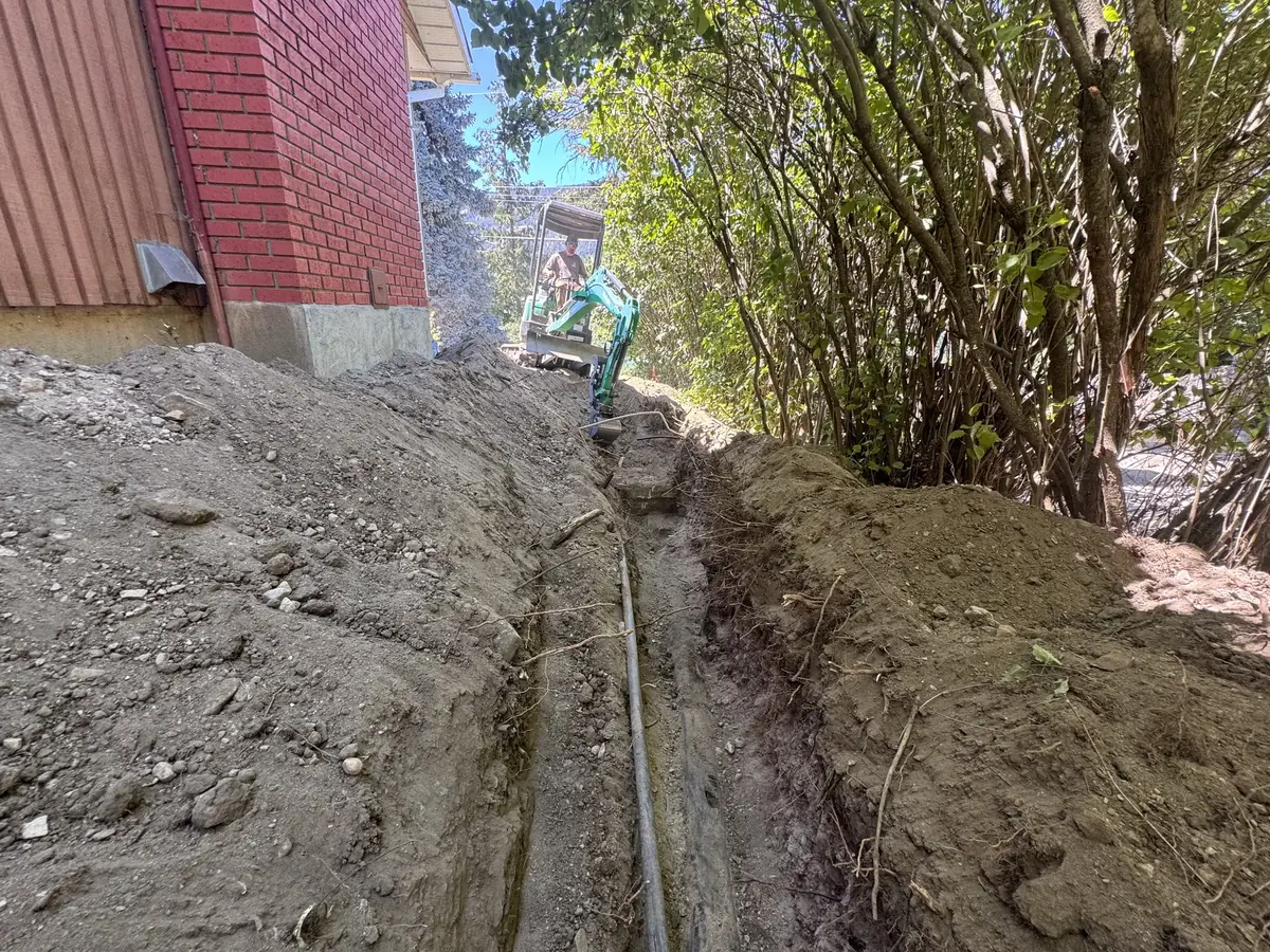 Compact excavator completing tight-access trenching beside a building
